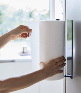 Side view of person grabbing paper towel from Black Magnetic Paper Towel Holder by Yamazaki Home. view 12