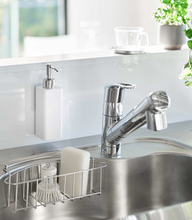 White Yamazaki Home square soap dispenser hooked in front of kitchen sink view 2