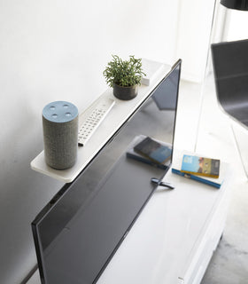 Aerial view of white Compliant TV Shelf holding smart home device, remote, and plant behind TV by Yamazaki Home. view 2