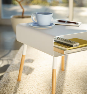 Close up view of white Storage Table holding cup, books, and remote by Yamazaki Home. view 6