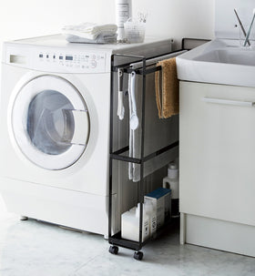 Black Rolling Towel Rack holding bath mats and cleaning products in laundry roomby Yamazaki Home. view 8