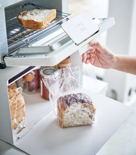 Close up side view of white Bread Box displaying bread and supporting toaster oven by Yamazaki Home. view 6