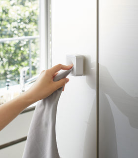 White Yamazaki Home Traceless Adhesive Towel Holder attached to a cabinet with a towel being inserted view 3