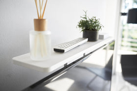 Close up view of white Compliant TV Shelf holding items behind TV by Yamazaki Home. view 5