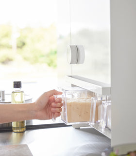 Image of a hand pulling out a container form the bottom shelf of the Concealable Spice Rack by Yamazaki Home in white. view 6