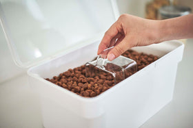 Close up view of person using clear measuring cup scooping pet food from white Airtight Food Storage Container by Yamazaki Home. view 5