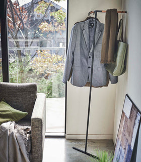 Yamazaki black Corner Leaning Coat Hanger placed in the corner of a room with items hung on it view 11