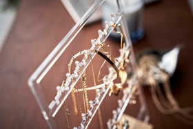 A detailed view of an acrylic translucent earring holder. The holder has upward pointed hooks and slots placed in an interchangeable pattern. Hanging from the hooks are chained necklaces, and in the slots are various earrings. view 6