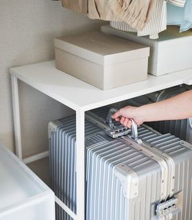 Close up of a suitcase being removed from underneath a white Yamazaki Home Expandable Suitcase Rack view 7