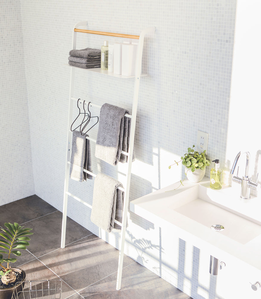 View 11 - White Leaning Ladder Rack holding containers, hangers, and cloth towels in bathroom by Yamazaki Home.