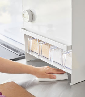 Image of a hand holding a duster and cleaning the countertop area under the Concealable Spice Rack by Yamazaki Home in white. view 5