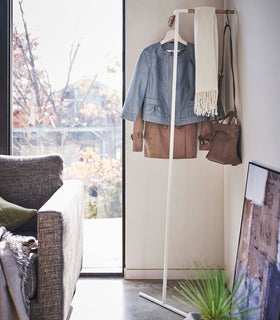 Yamazaki white Corner Leaning Coat Hanger in a the corner of a room with clothing hung on it view 3