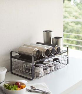 Black Expandable Countertop Organizer expanded holding bottles on kitchen countertop by Yamazaki Home. view 9