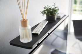 Close up view of black Compliant TV Shelf holding items behind TV by Yamazaki Home. view 8