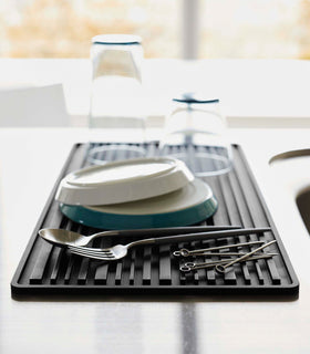 Close up of black Yamazaki Roll-Up Dish Drying Mat next to a kitchen sink with dishes drying on top view 13