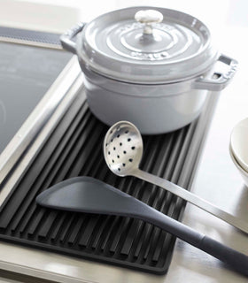 Close up of black Yamazaki Roll-Up Dish Drying Mat next to a kitchen stove with a dutch oven and utensils on top view 14