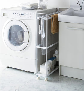 Side view of white Rolling Towel Rack holding towel and cleaning products in laundry room by Yamazaki Home. view 3