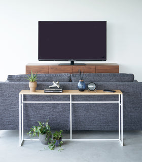 Straight view of the Long Console Table by Yamazaki Home in white with decorative items placed behind a gray couch in a living room. view 4