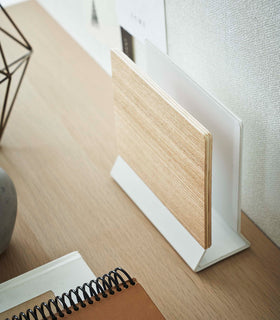 A side-view profile of a narrow wooden stand with a white metal base positioned by books on top of a desk. view 8